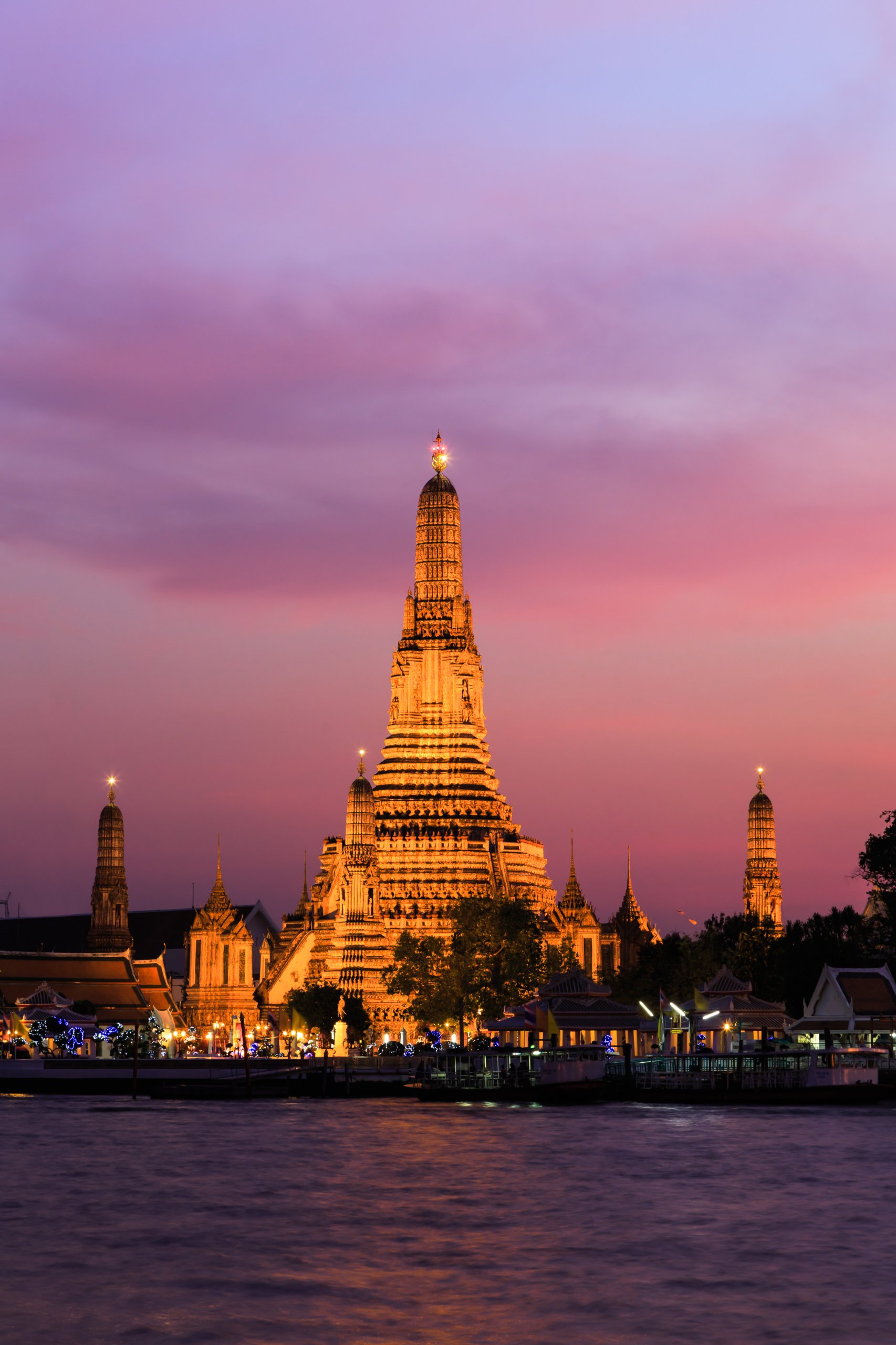 Templo Wat Arun iluminado ao anoitecer, na margem do rio Chao Phraya, em Banguecoque