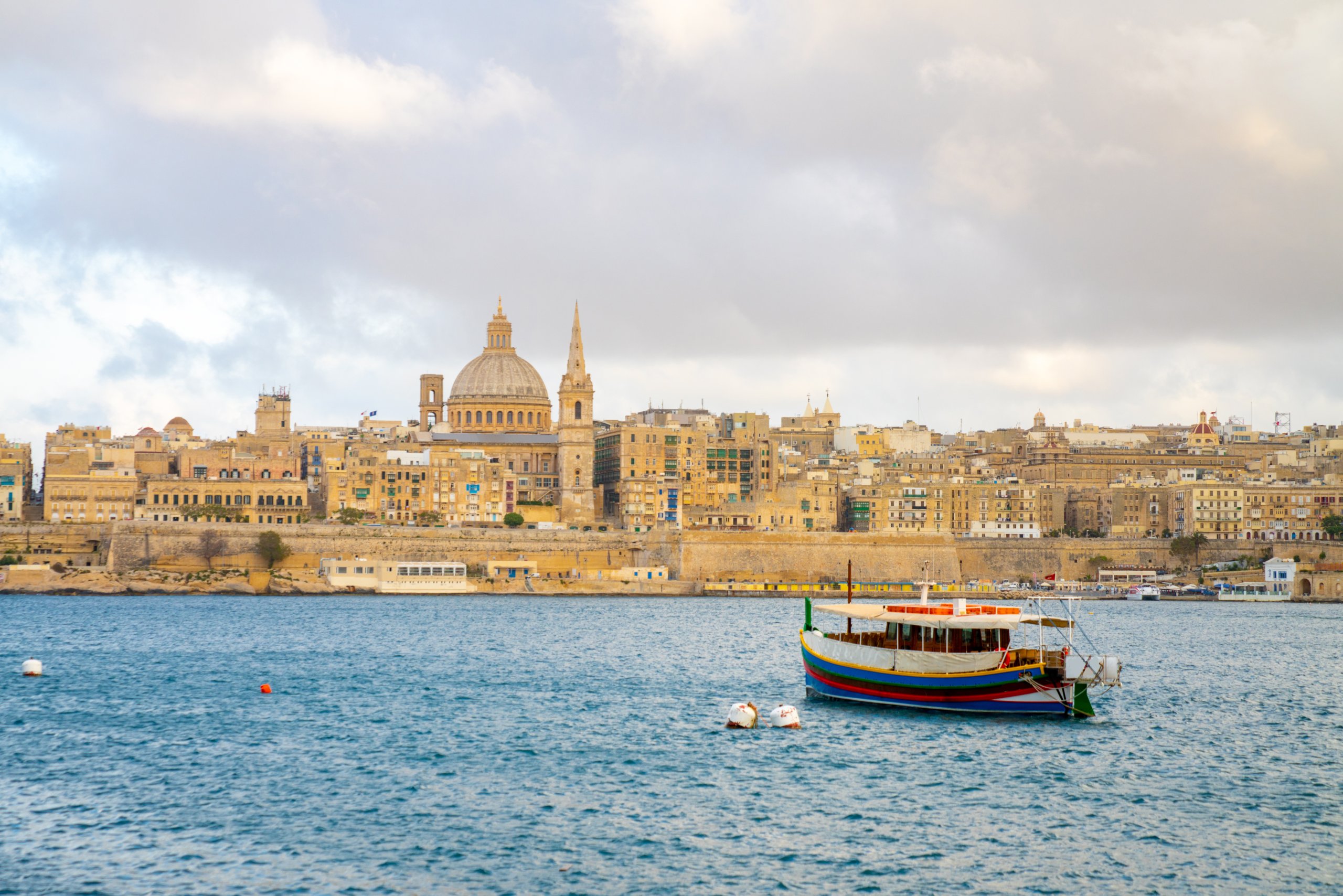 La Valletta vista do outro lado do porto, com a cúpula da basílica e um barco tradicional